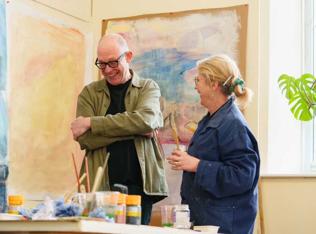 Art teacher and student smiling together, with paints and brushes in the foreground Art teacher and student smiling together, with paints and brushes in the foreground
